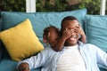 African American father playing peek a boo with his little daughter while spending happy time together at home on couch Royalty Free Stock Photo