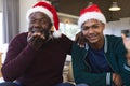 African american father and son in christmas hats having video call, waving, blowing kiss Royalty Free Stock Photo