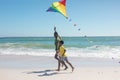 African american father and son holding hands while running with kite at beach on sunny day Royalty Free Stock Photo