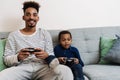 African american father and son playing video game while sitting on couch Royalty Free Stock Photo