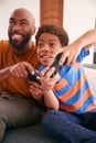 African American Father And Son Sitting On Sofa At Home Playing Video Game Together Royalty Free Stock Photo