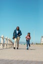 African american father walking by son riding push scooter on promenade against clear blue sky