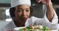 African american female chef garnishing dish and similing in restaurant kitchen