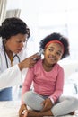 African american female doctor examining girl patient using otoscopy at hospital