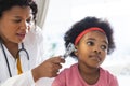 African american female doctor examining girl patient using otoscopy at hospital