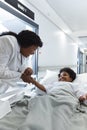 African american female doctor talking to girl patient lying on bed in corridor at hospital Royalty Free Stock Photo