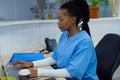 African american female doctor wearing scrubs sitting at reception desk at hospital Royalty Free Stock Photo