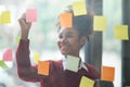 African American female employee write down on colorful sticky notes manage list, concentrated biracial woman work on