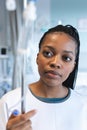 African american female patient wearing hospital gown, holding drip in hospital room Royalty Free Stock Photo