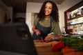 African American female smiling chopping vegetables looking at videos on digital tablet
