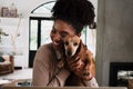 African American female smiling while snuggling cute puppy sitting at desk in modern kitchen. Royalty Free Stock Photo