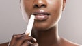 Black woman applying lip balm over grey background, closeup