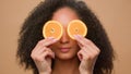 African American girl covering eyes with slices of citrus peeping blink eye woman hold two half of orange cosmetology Royalty Free Stock Photo