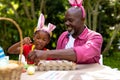 African american girl and grandfather wearing bunny ears while painting eggs on easter day