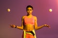 African american girl in pink sports bra and shorts juggle with balls on purple background with gradient Royalty Free Stock Photo