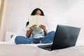 African american girl student doing homework or preparing to exams in bed at home, using laptop pc and hiding her face Royalty Free Stock Photo