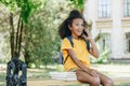 African american girl talking on smartphone while sitting on bench near books and apple Royalty Free Stock Photo