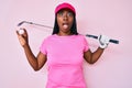 African american golfer woman with braids holding golf ball afraid and shocked with surprise and amazed expression, fear and Royalty Free Stock Photo
