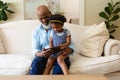 African american grandfather and granddaughter using digital tablet sitting on couch at home Royalty Free Stock Photo