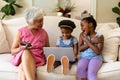 African american grandmother and her two granddaughters using laptop sitting on couch at home Royalty Free Stock Photo