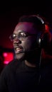 An african-american guy with glasses and a headset plays on the computer and talks, gives hints to the team, smiles