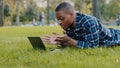 African american guy young business man user lying on green grass lawn in park using laptop online call conference chat Royalty Free Stock Photo