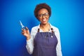 African american hairdresser woman holding scissors over blue isolated background with a happy face standing and smiling with a