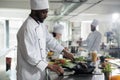 African american head cook searing succulent beef patty while preparing food for dinner service at restaurant.