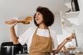 African american housewife in apron singing with spatulas for cooking microphone on the kitchen. Joyful African young Royalty Free Stock Photo