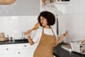 African american housewife in apron singing with spatulas for cooking microphone on the kitchen. Joyful African young Royalty Free Stock Photo