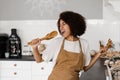 African american housewife in apron singing with spatulas for cooking microphone on the kitchen. Joyful African young Royalty Free Stock Photo