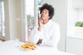 African American hungry man eating hamburger for lunch with hand on chin thinking about question, pensive expression