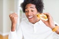 African American hungry man eating hamburger for lunch screaming proud and celebrating victory and success very excited, cheering Royalty Free Stock Photo