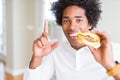 African American hungry man eating hamburger for lunch surprised with an idea or question pointing finger with happy face, number