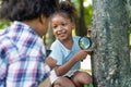 African American little girls with friends exploring and looking bugs on the tree with the magnifying glass between learning Royalty Free Stock Photo