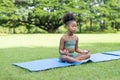 African American little girl sitting with closed eyes practicing meditate yoga on roll mat in the park Royalty Free Stock Photo