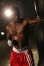 African American male boxer hitting punch bag in red shorts at the gym