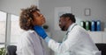 African-American male doctor palpating throat of woman examining female patient during consultation in clinic Royalty Free Stock Photo