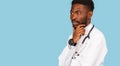 African american male doctor with stethoscope holds hand to chin and thinks over blue background Royalty Free Stock Photo