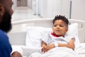 African american male doctor talking to boy patient in hospital bed in corridor with copy space Royalty Free Stock Photo