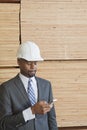 African American male engineer using cell phone with stacked wooden planks in background Royalty Free Stock Photo