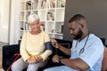 African american male health worker checking blood pressure of caucasian senior woman at home