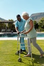 African american male health worker helping caucasian senior woman to walk with a walking frame