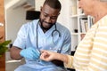 African american male health worker measuring blood sugar of caucasian senior woman using glucometer