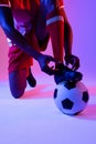 African american male soccer player with football tying shoes over neon pink lighting