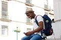 African american male tourist sitting outside with bag and mobile phone Royalty Free Stock Photo