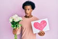 African american man with afro hair bouquet of flowers and heart draw for anniversary clueless and confused expression