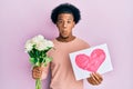 African american man with afro hair bouquet of flowers and heart draw for anniversary puffing cheeks with funny face