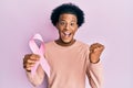 African american man with afro hair holding pink cancer ribbon screaming proud, celebrating victory and success very excited with Royalty Free Stock Photo