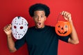 African american man with afro hair wearing hockey mask and halloween pumpking afraid and shocked with surprise and amazed